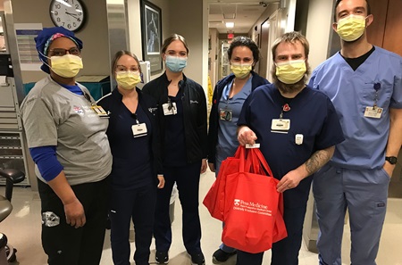 Group of hospital workers wearing scrubs hold red bags of donated toiletries for patients.